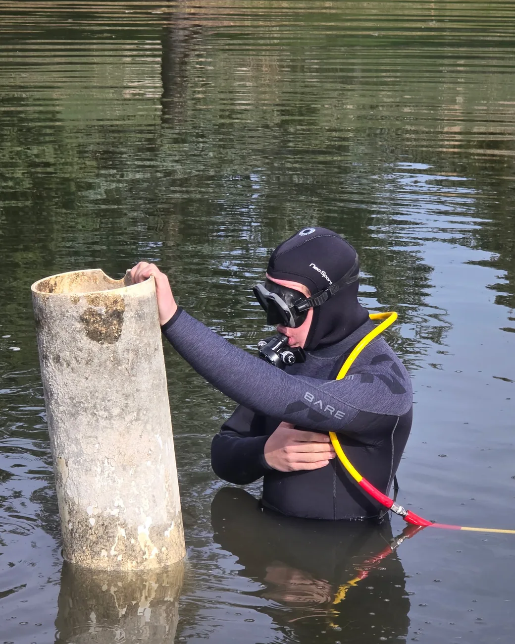 Diver in a hood and mask working on a submerged pipe