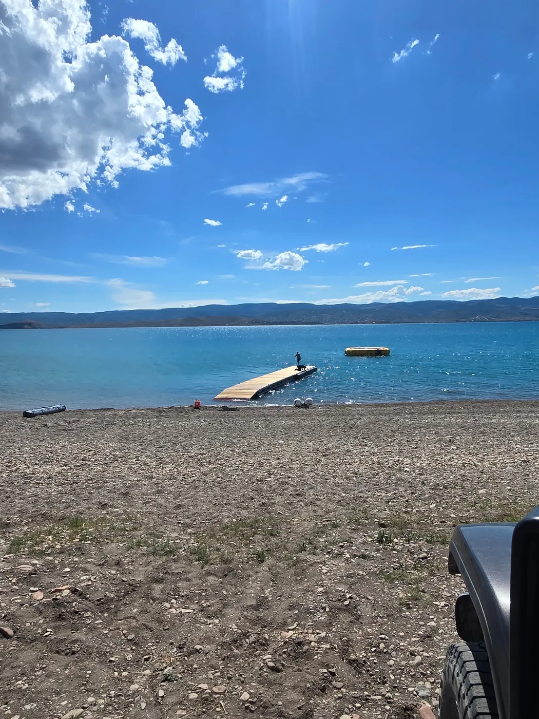 Floating dock off a gravel beach on a bright day, open lake behind it