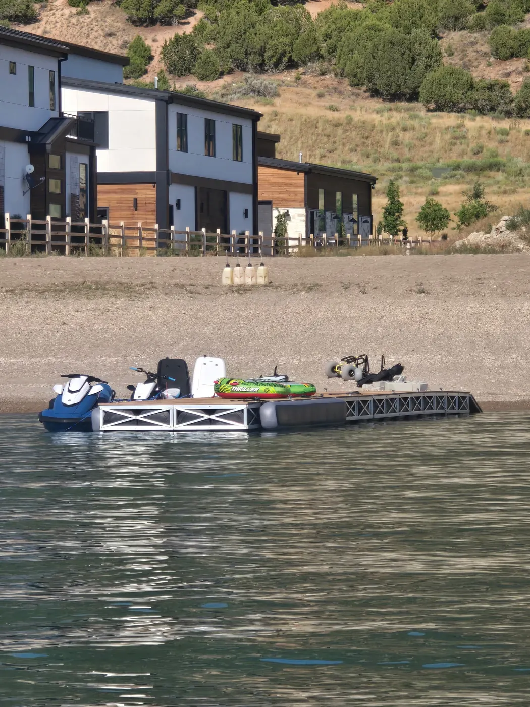 Floating dock loaded with personal watercraft and tubes in front of lakefront homes