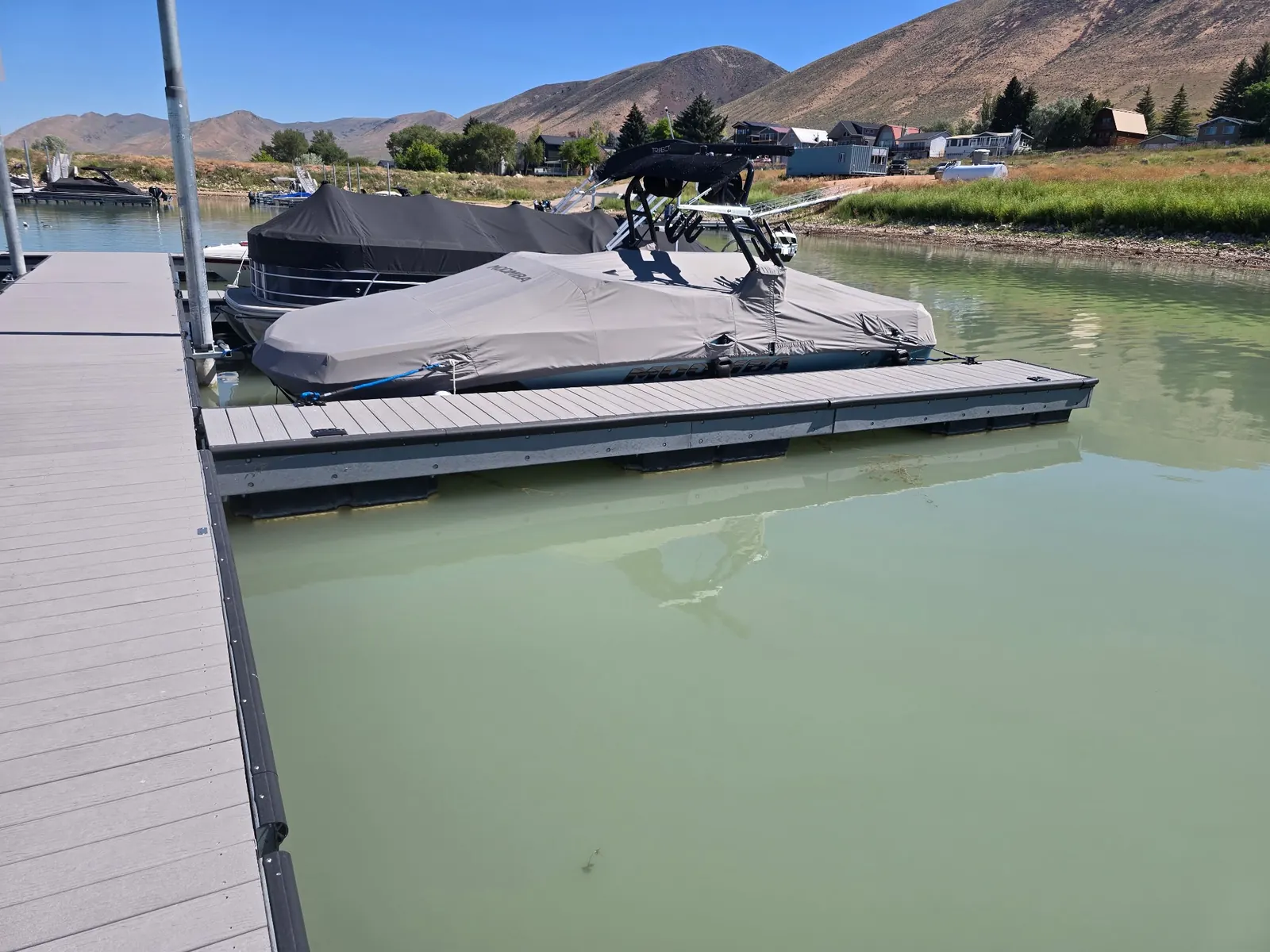 Covered boat tied up in a floating slip at a Bear Lake marina, mountains behind