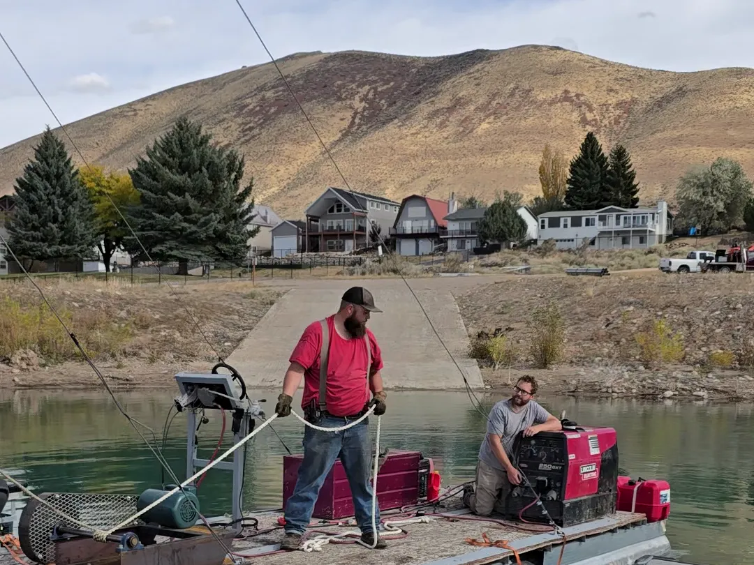 Crew running the pile driving rig from a work barge on Bear Lake, hills behind